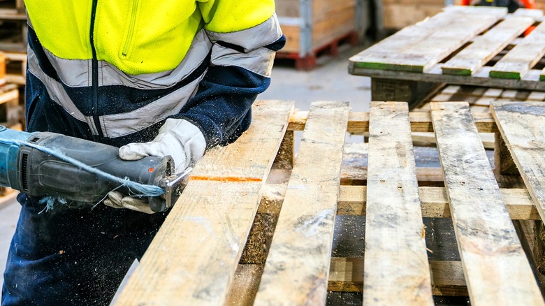 Close-up of a person in a warehouse cutting a pallet with a saw