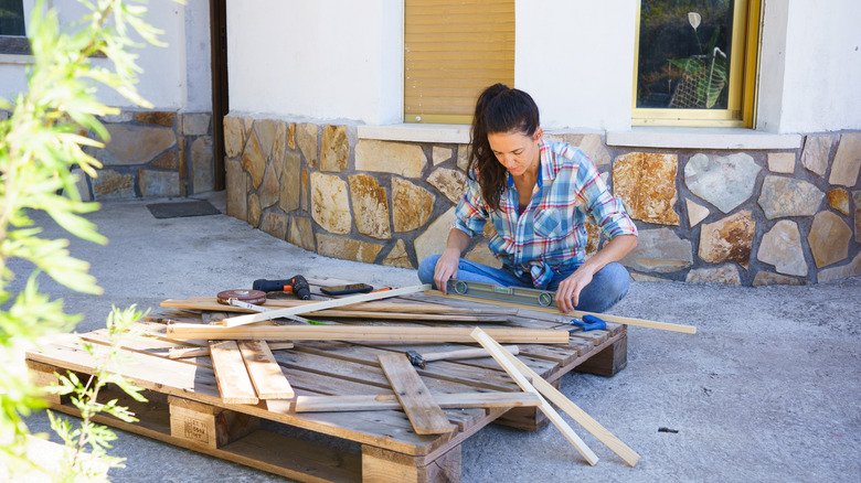 Woman breaking down a wood pallet in her backyard.