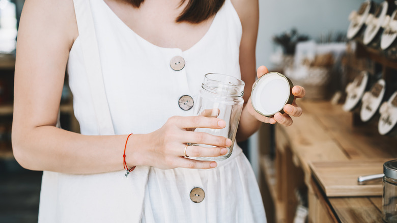 A woman in a white dress holding an empty glass jar.
