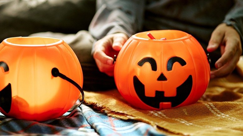 Close-up of two empty Halloween jack-o'-lantern buckets with a person sitting behind the one on the right