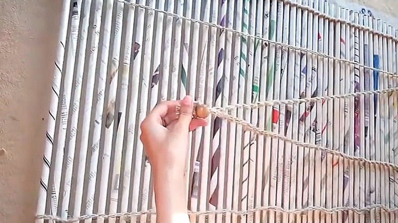 Person shows bead holder for the cord of a DIY curtain made out of newspaper rolls