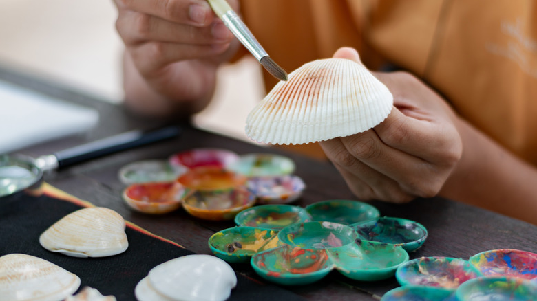 A person paints a seashell brown using a small paintbrush.