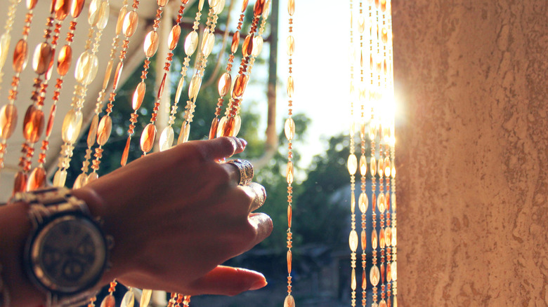 Persons hand pulling open a glass beaded curtain.