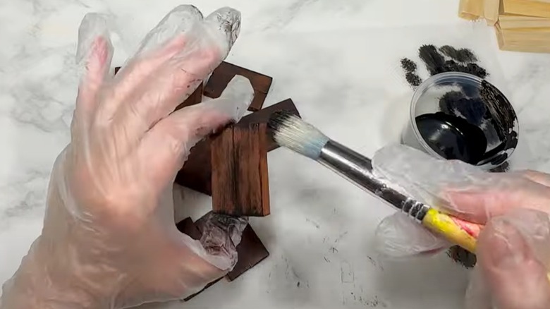 Two gloved hands work on painting wooden blocks.