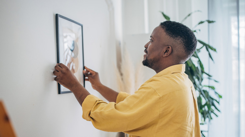 An African American man hangs a framed art piece on a wall.