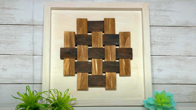 A wooden woven-look art piece leans against a wall from a shelf.