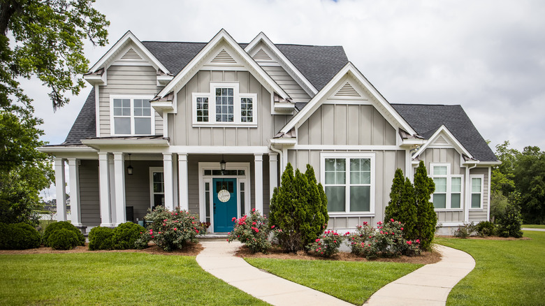 Evergreen trees and pink knockout roses are planted in front of a gray two-story house