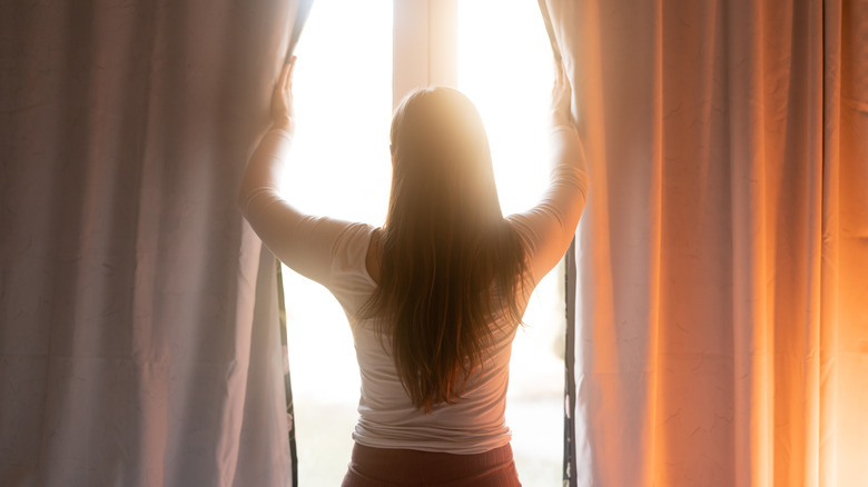 woman opening curtains