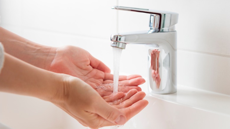 Hands reflected in chrome faucet while washing them