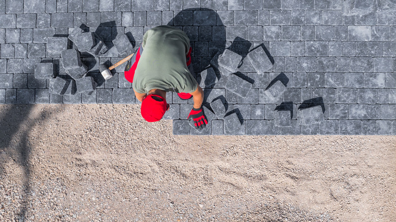 A worker carefully installs pavers in a residential backyard