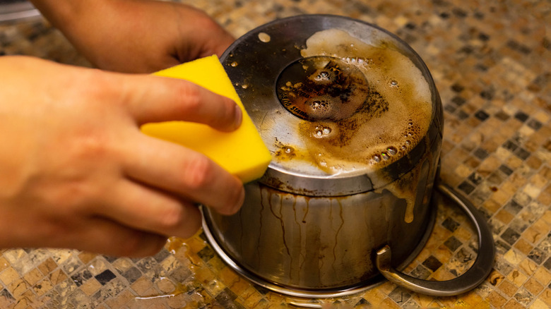 man scrubbing the bottom of a greasy pan