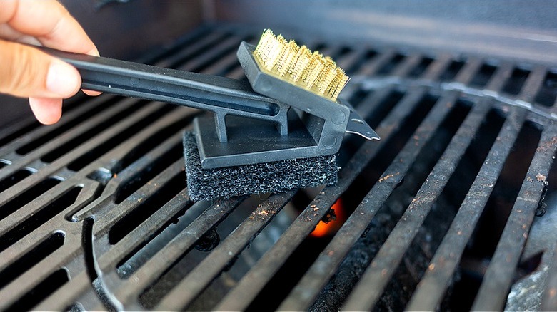 Person cleaning grill with a scraper brush
