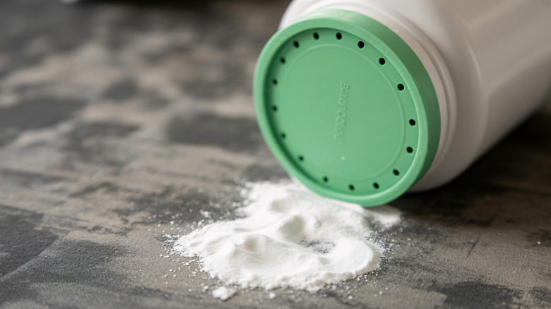 Baby powder spilled on a carpet next to a tipped over bottle