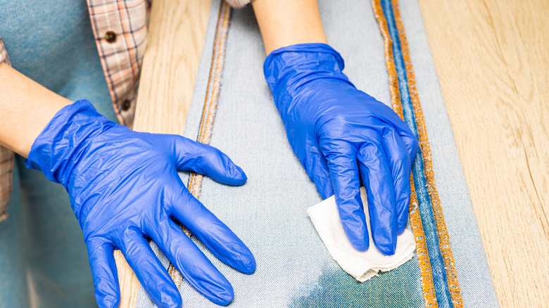 person with a gloved hands applying stain removal to denim jeans