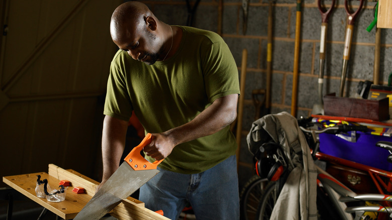 A man uses a manual saw in a home workshop.