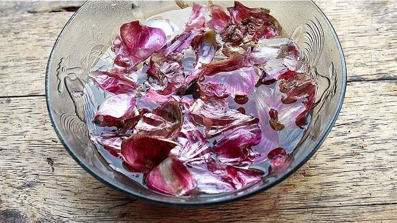 Bowl of red onion peels soaking in water on a wood surface