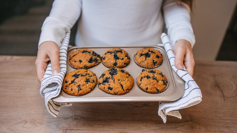 person holding baked muffins in a muffin tin