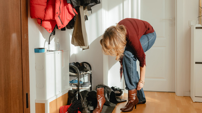 A woman putting on boots in an entryway with storage