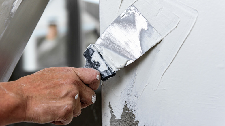 A putty knife used to flatten white plaster on a wall