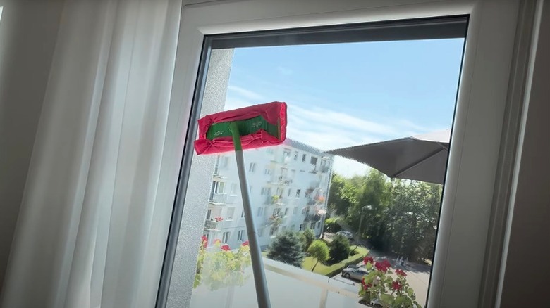 Woman cleaning tall window with Swiffer and cloth