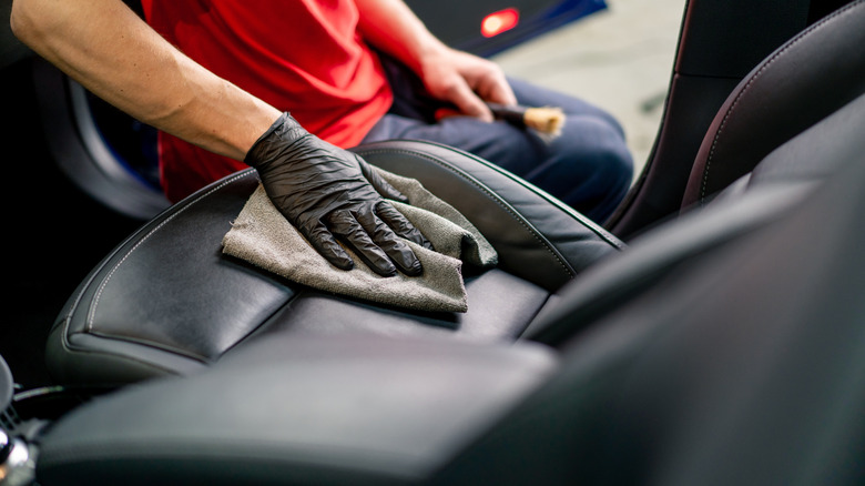 Man using old towel for detailing leather seat in car