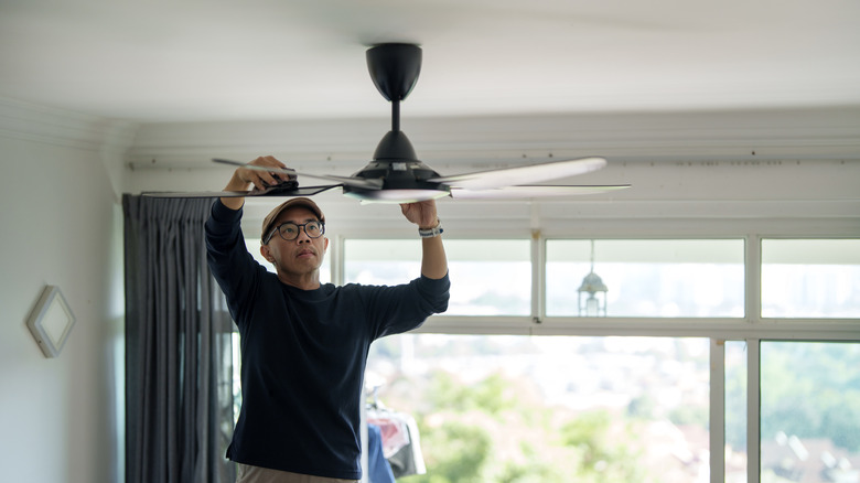Man cleaning ceiling fan blade with a cloth