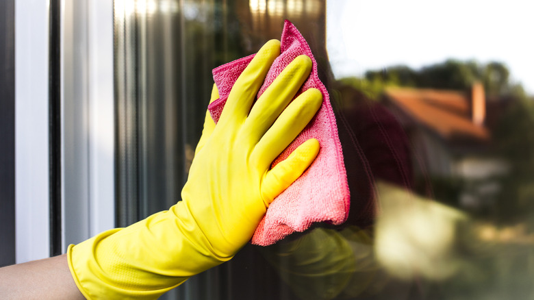 A yellow gloved hand wiping window with pink cloth