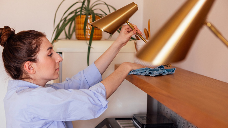 Woman using blue cloth to dust shelf