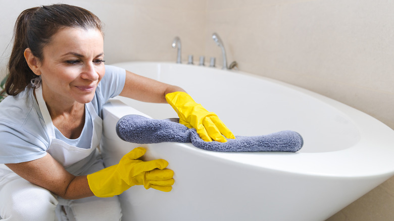 Woman cleaning a tub with a blue towel