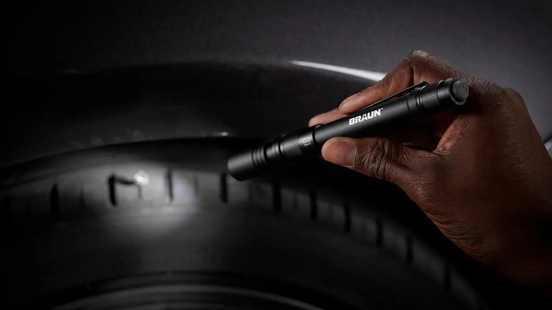 Person using BRAUN 450 Lumen Rechargeable Penlight to examine tire