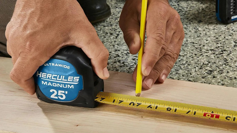 Person using HERCULES 25-Foot Magnetic Tape Measure to measure wood plank