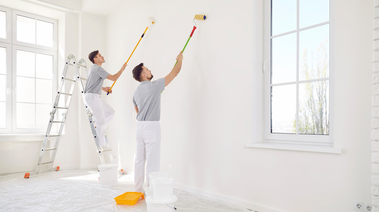 Two men rolling paint finish onto walls in an unfurnished, brightly lit room.