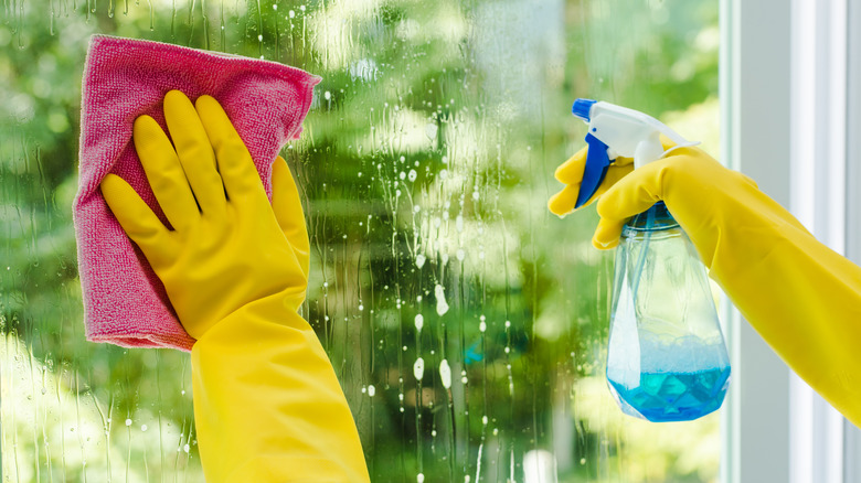 hands cleaning window with cleaner