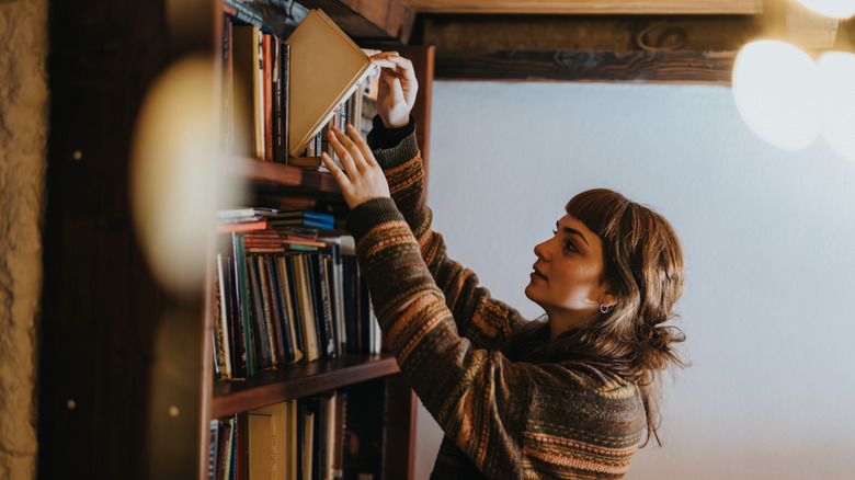 A woman pulls a book from a bookshelf