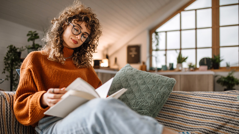 A woman sits in a cozy attic space reading a book