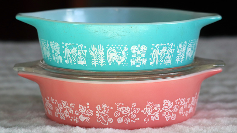 Two vintage milk-glass one-pint casserole dishes stacked on top of each other. One is aqua blue with an Amish pattern. One is pink with a gooseberry pattern.