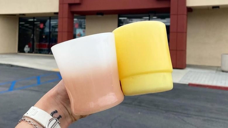 Hand holding up two Fire-King mugs outside of a thrift store entrance