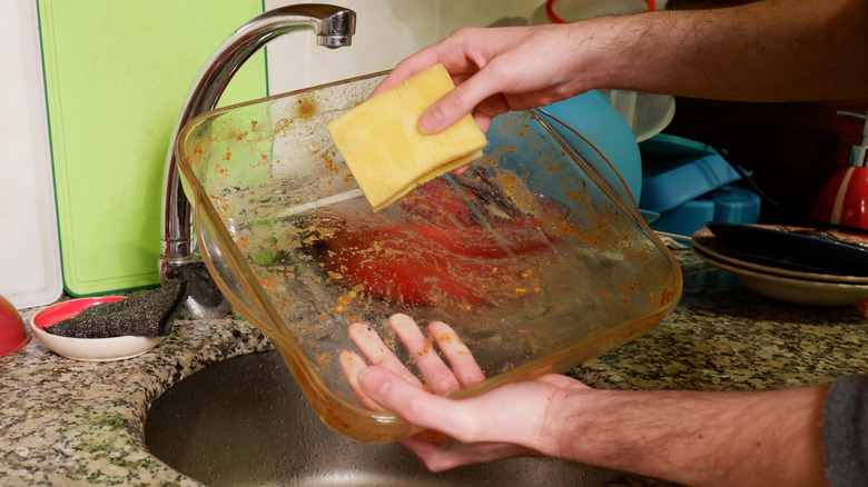 Person cleaning a greasy casserole dish with a sponge