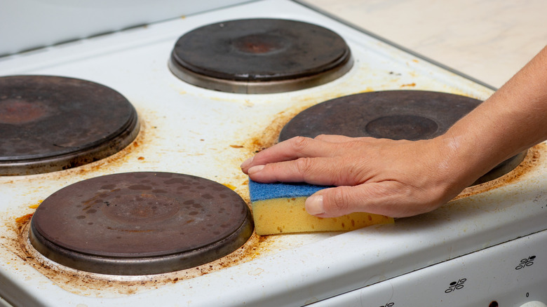 Person cleans a filthy stovetop with a sponge