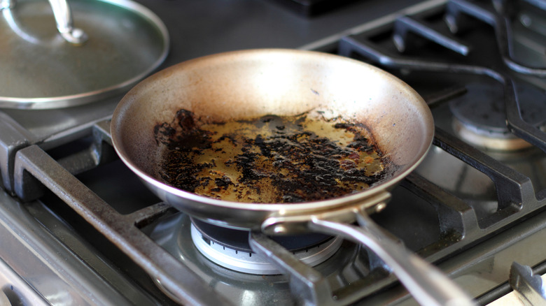A greasy and charred pan sits on a stove