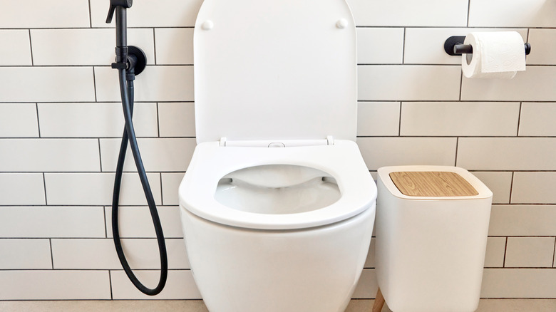 A trash can sitting next to a toilet in a bathroom