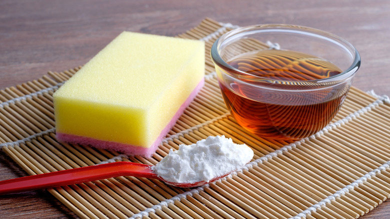 Apple cider vinegar in a bowl with a sponge and spoon of baking soda