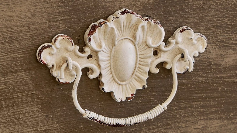 A white vintage drawer pull against wood.