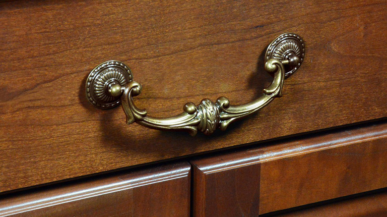 A brass victorian pull on a wood drawer.