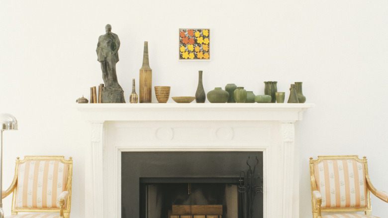 Fireplace with white mantelpiece adorned with green ceramics and a small stone sculpture.