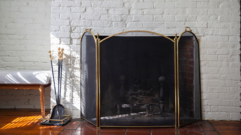 Fireplace with black fire guard screen and tools like shovel and poker. White brick wall