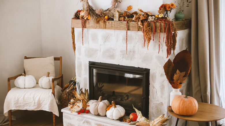 Stylish autumn decor of fireplace mantel in living room. Pumpkins, autumn leaves, nuts, candle on rustic wood on fireplace. Fall season decoration. Thanksgiving and Halloween
