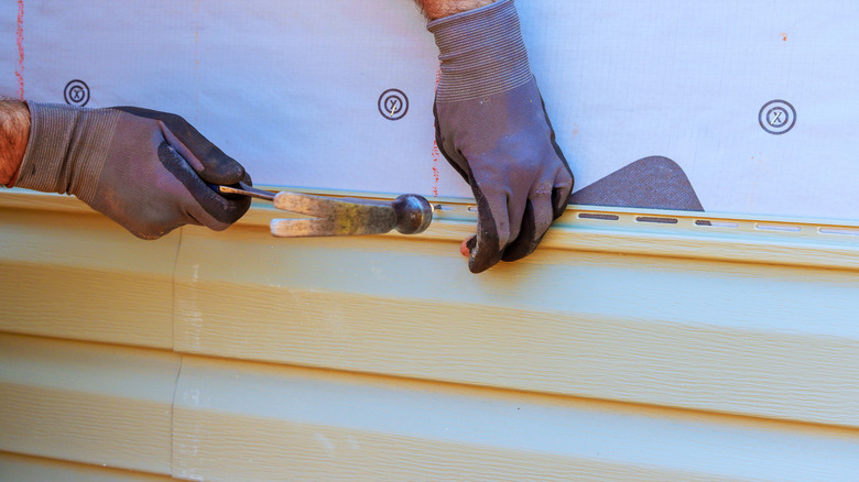 Someone hammering a piece of cream colored siding on an unfinished house.