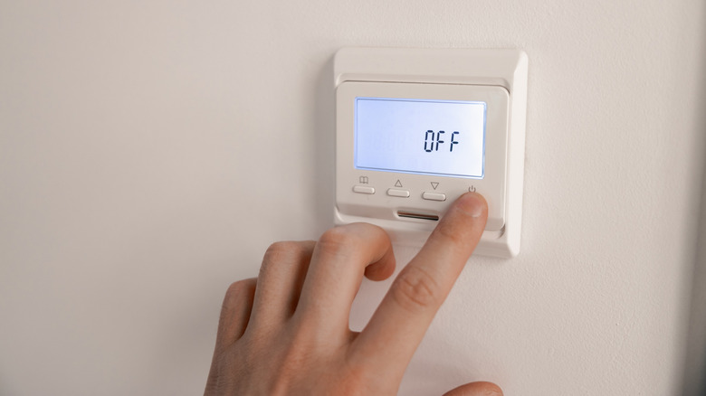 A person pushes the "Off" button on a wall-mounted thermostat