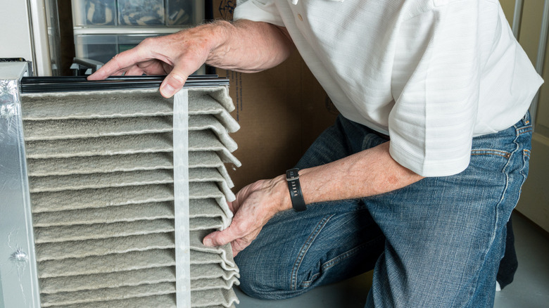 A man kneels while pulling a dirty filter out of a furnace